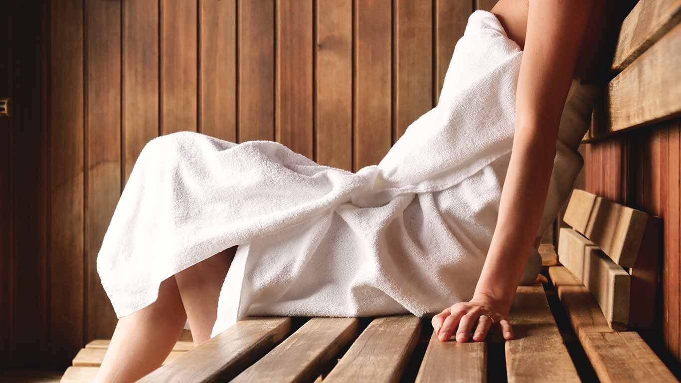 Een vrouw in een handdoek ligt te ontspannen in de sauna. 